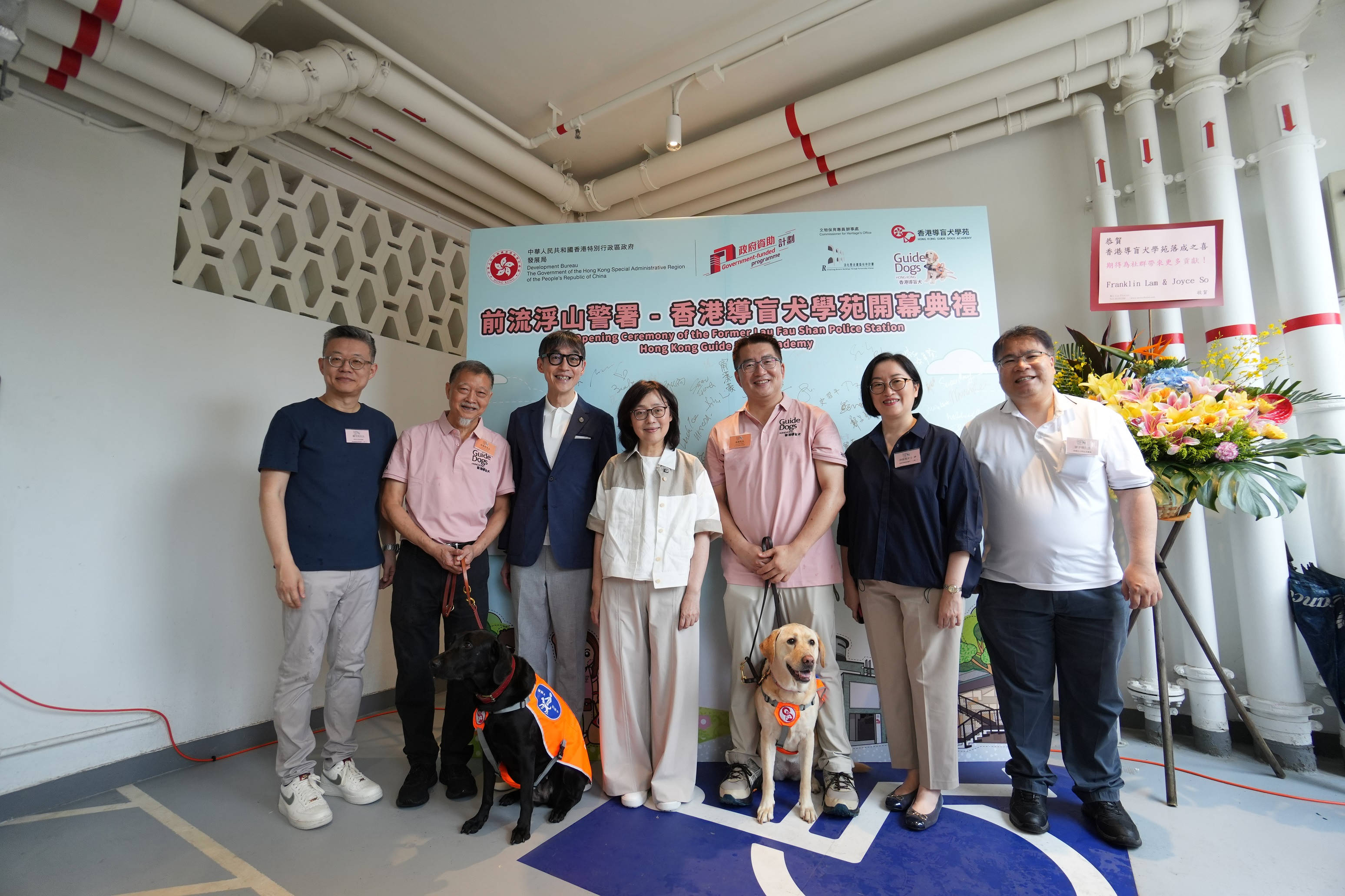 發展局局長甯漢豪（後排中）主持前流浮山警署－香港導盲犬學苑開幕典禮，與其他主禮嘉賓，包括保育歷史建築諮詢委員會主席蘇彰德教授（後排左三）、香港導盲犬協會主席胡鍔（後排右三）和傳訊及籌款委員會主席林衛邦（後排左二），以及導盲犬Alya （前排右）和治療犬Zita （前排左）合照。